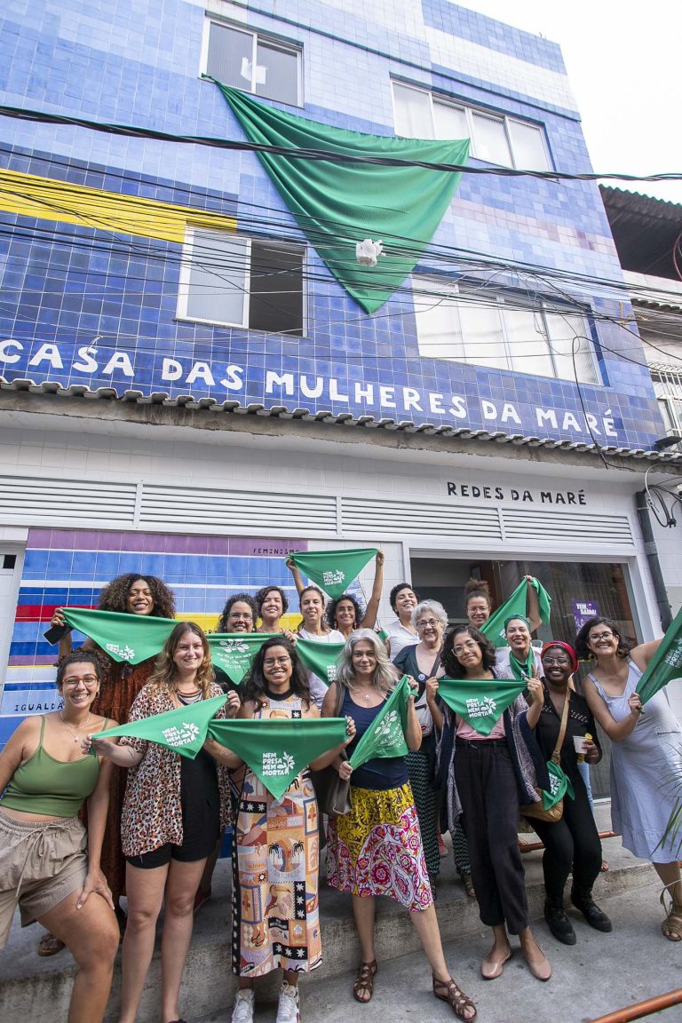 Várias mulheres seguram lenços verdes em frente à Casa das Mulheres da Maré.