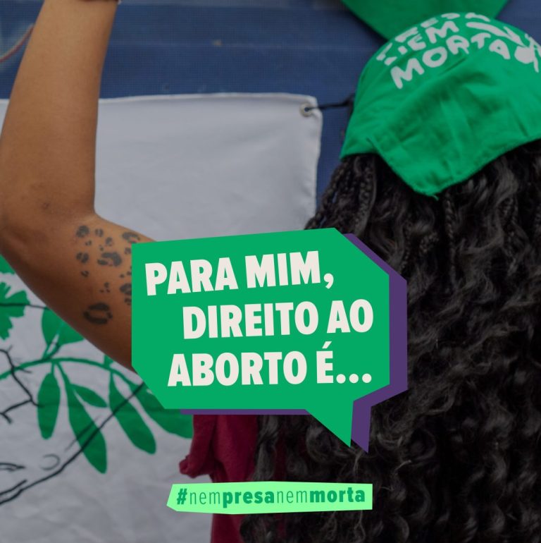 Foto de uma mulher de costas com uma bandana verde da NPNM sobre os cabelos pretos cacheados. Ela está de punho erguido. No centro, lê-se: Para mim direito ao aborto é… Assina Nem Presa Nem Morta.