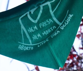 Ienço verde pendurado, com ilustração de uma mulher e dizendo: "nem presa, nem morta, aborto livre para decidir".
