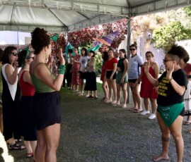 Mulheres em duas filas, uma de frente pra outra fazendo atividades corporais.