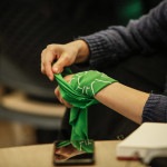 Foto Alexa Rochi. Mulher branca enrola lenço verde no pulso.