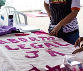 Foto: Mídia Ninja. Pessoas trabalham sobre uma mesa montando cartaz que diz: Aborto Legal Já.