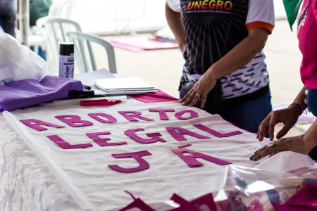 Foto: Mídia Ninja. Pessoas trabalham sobre uma mesa montando cartaz que diz: Aborto Legal Já.