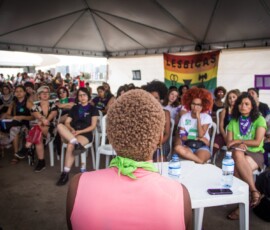 Foto: Mídia Ninja. Plateia ouve uma mulher negra de cabelos curtos, que aparece em primeiro plano, de costas na foto.