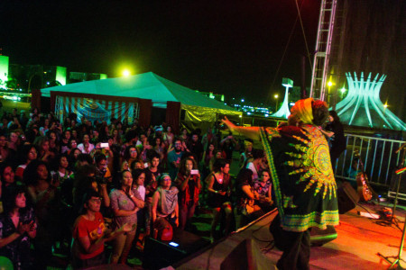 Foto: Mídia Ninja. Em cima o palco uma artista negra faz show para uma plateia à noite