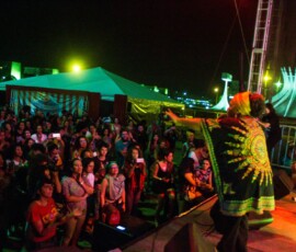 Foto: Mídia Ninja. Em cima o palco uma artista negra faz show para uma plateia à noite