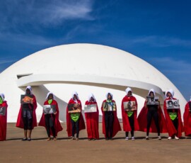 10 mulheres vestidas como "aias" do livro "o conto da aia" seguram cartazes em Brasília.