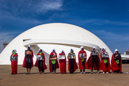 10 mulheres vestidas como "aias" do livro "o conto da aia" seguram cartazes em Brasília.