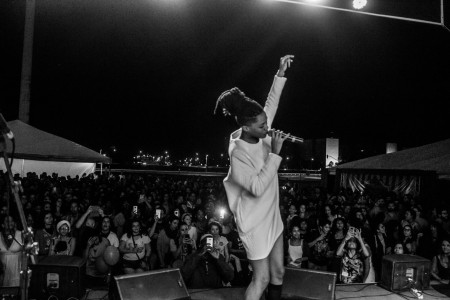 Foto: Mídia Ninja. Foto de cima de um palco. Mulher negra com o braço erguido canta para uma planteia. Foto em preto e branco.