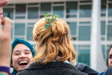 Foto: Chama. Foto de costas de uma mulher com cabelos ruivos, com um ramo de arruda preso ao cabelo.