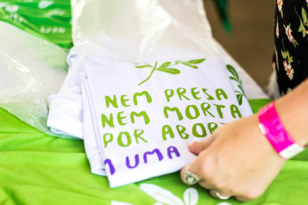 Foto: Mídia Ninja. Camisetas dobradas em cima de uma mesa com estampa: Nem presa Nem Morta por aborto.