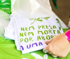 Foto: Mídia Ninja. Camisetas dobradas em cima de uma mesa com estampa: Nem presa Nem Morta por aborto.