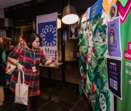 Mulher de casaco vermelho quadriculado fotografa painel que expõe lenços verdes e cartazes da campanha Causa Justa.
