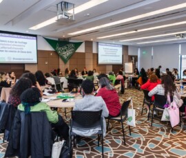 Participantes estão divididas em mesas circulares na sala de reunião.