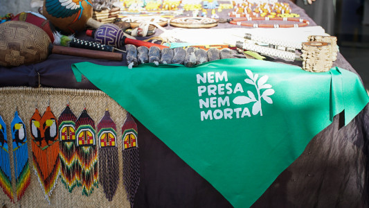 Mesa com artesanato indígena e um lenço verde Nem Presa Nem Morta.