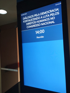 Placa da sessão da câmara ddos deputados one lê-se: "Diálogos pela Democracia: Fortalecendo a luta pelos Direitos Humanos no Congresso Nacional", 14:00".