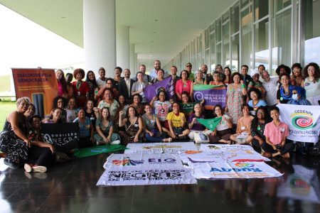Pessoas posam juntas em meio a bandeiras e estandartes de movimentos sociais e organizações não-governamentais.