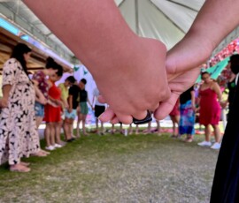 Mulheres de mãos dadas fazem uma roda. Em primeiro plano duas mãos dadas.