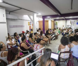Mulheres estão sentadas em cadeiras em uma sala com cartazes nas paredes.