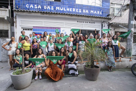 Participantes, palestrantes e coordenadoras da Roda de Conversa posam em frente à Casa das Mulheres da Maré. Foto: Gabi Lino. Grupo de mulheres seguram lenços verdes da Campanha Nem Presa Nem Morta em frente à Casa das Mulheres da Maré.