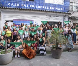 Grupo de mulheres seguram lenços verdes da Campanha Nem Presa Nem Morta em frente à Casa das Mulheres da Maré.