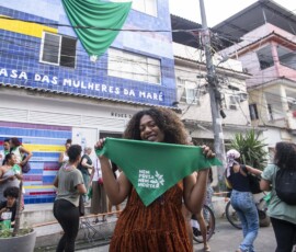 Mulher negra segura lenço verde da Campanha Nem Presa Nem Morta em frente à Casa das Mulheres da Maré.
