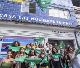 Várias mulheres seguram lenços verdes em frente à Casa das Mulheres da Maré.