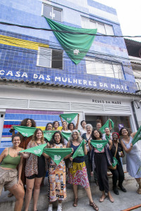 Grupo coordenador e palestrantes da Roda de Conversa na Casa das Mulheres da Maré. Foto: Gabi Lino Várias mulheres seguram lenços verdes em frente à Casa das Mulheres da Maré.