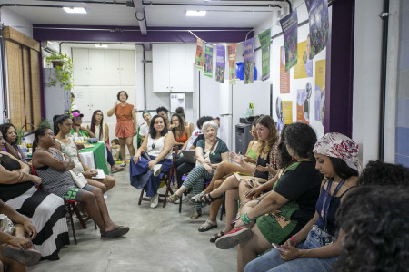 Em sua fala Bibiana Serpa informou sobre a ADPF 442 e a necessária união de forças pela legalização do aborto no país. Foto: Gabi Lino Mulheres estão sentadas em cadeiras em uma sala com cartazes nas paredes.