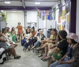 Mulheres estão sentadas em cadeiras em uma sala com cartazes nas paredes.