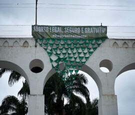 Os Arcos da Lapa, cartão postal do Rio de Janeiro, amanheceram no dia 28 de Setembro emoldurando uma grande banderia confeccionada com lenços verdes da Campanha Nem Presa Nem Morta e uma mensagem uníssona: Aborto legal, seguro e gratuito! Foto: Marina Laiun. Foto dos arcos da lapa, no Rio de janeiro. Há uma faixa verde que diz "Aborto legal, seguro e gratuito. Descriminaliza STF". Abaixo há uma bandeira formada por diversos lenços unidos pelas pontas, que formam um triângulo.