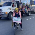 O artivismo animou e coloriu a Marcha pelo Fim da Violência de Gênero. Foto: equipe NPNM. Uma pessoa mascarada com adereço de onça está em uma bicicleta com um cartaz onde se lê, em espanhol: Cada fronteira no mundo é uma cicatriz. Ao fundo há um caminhão com a caçamba cheia de ativistas.