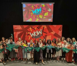 Diversas pessoas seguram lenços verdes em um paco com o fundo do festival mulheres do mundo, em vermelho.