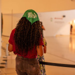 Festival WOW: recepcionista aderiu ao lenço verde. Foto: Mari Bley. Mulher aparece de costas e tem o lenço da campanha nem presa nem morta amarrando os cabelos cacheados e compridos.