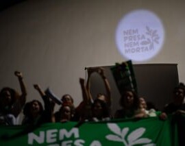 Foto de uma projeção feita na cúpula do Museu Nacional da República onde se lê: Nem Presa Nem Morta. Na frente, há mulheres de braços erguidos com um lenço gigante verde.