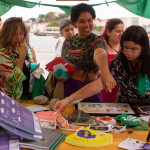 Festival WOW - Barraca aborteira movimentou a feira: muito diálogo rolou por lá! Foto: Mari Bley. Foto de uma mesa, que fazia parte da barraca de Justiça Reprodutiva, onde á materiais diversos dispostos. Algumas mulheres observam e pegam os materiais que estão sobre a mesa.