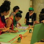 Na programação do evento, houve tempo de preparação para a manifestação do dia 28 de setembro, dia latinoamericano de luta pela descriminalização do aborto. Foto: Daniele Fagundes. Fotos de mulheres trabalhando sobre uma mesa. Elas pintam cartazes com pinceis e tintas.
