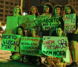 Oito mulheres seguram cartazes com frases que pedem a descriminalização das mulheres e a legalização do aborto.