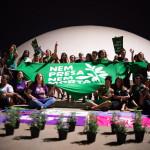 Grupo participante do ato noturno, no Museu Nacional da República. Foto: Andressa Anholete. Foto de mulheres segurando um lenço verde gigante na frente do Museu Nacional da República. Em primeiro plano, várias mudas de arrudas estão dispostas.