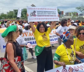 Foto das mulheres em marcha com faixas e lenços verdes. Ao centro, uma delas ergue um banner por justiça reprodutiva.
