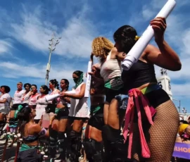 Foto com mulheres em passeata que se equilibram em pernas de pau.
