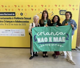 Foto do painel amarelo da Semana Nacional de Enfrentamento da Violência Sexual contra Crianças e Adoslescentes. Ao lado, quatro ativistas posam pra foto segurando a bandeira da campanha Criança Não é Mãe.