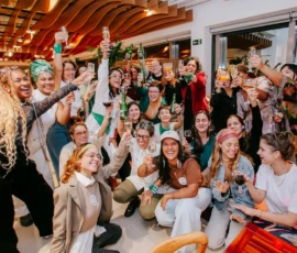 Foto das participantes, convidadas e equipe brindando com taças e garrafas erguidas.
