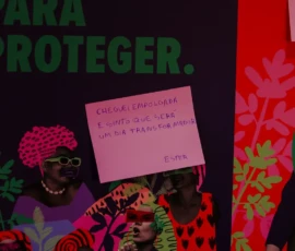 Fotos de um postit rosa, com o texto: Cheguei empolgada e sinto que será um dia transformador - Ester. Ele está sobre um cartaz colorido.