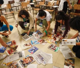 Foto das participantes agachadas olhando e pegando revistas que estão no chão.