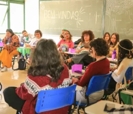 Foto da sala com participantes da ativdade sentadas. Atrás delas um quadro verde escrito em giz branco: Bem-vindas.