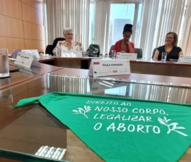 Acervo Ministério das Mulheres Foto da mesa de reunião com a Ministra Cida Gonçalves e quatro ativistas. Em primeiro plano, um lenço verde com o texto: Direito ao nosso corpo. Legalizar o aborto.