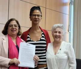 Acervo Ministério das Mulheres Foto da Ministra Cida Gonçalves posando pra câmera com um documento. Ao seu lado, as ativistas Joluzia Batista e Angela Freitas, sorriem.