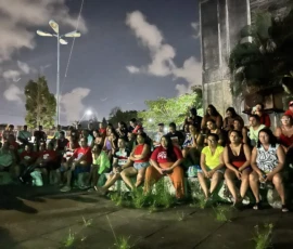 Foto de pessoas sentadas numa arquibancada ao ar livre, à noite, na Universidade Federal de Pernambuco.