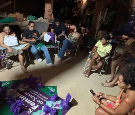Foto de pessoas sentadas em círculo, no meio bandeiras e lenços verdes.